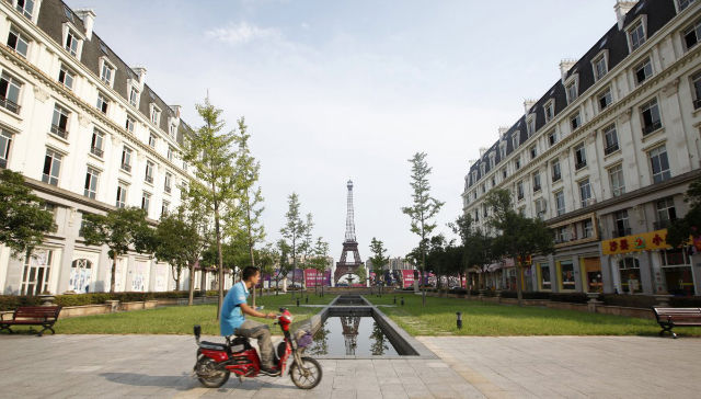 A man rides a motorcycle past a replica of the Eiffel Tower
