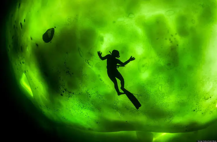 Diver beneath thick ice, Northern Lights