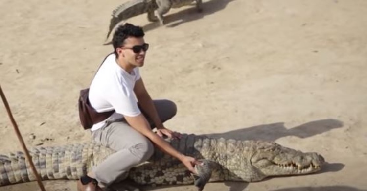 A man is sitting on a crocodile in an African village